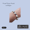 A close-up of a person's wrist wearing a beaded bracelet made of large white freshwater pearls and small dark blue beads, on a light blue background with the text 'Fresh Water Pearls and Lapis' and the brand name 'Sseau Beautiful by Heather'