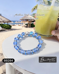 Blue beaded bracelet on a table with a beach setting and a drink in the background