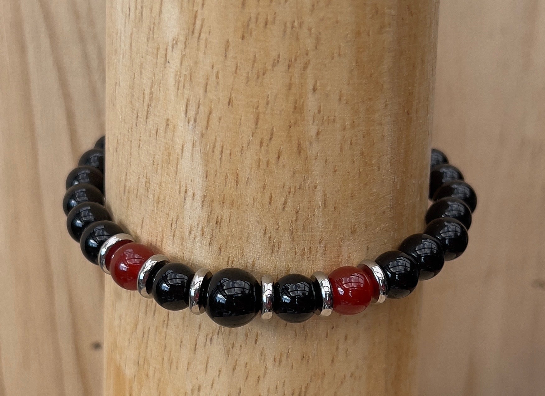 Beaded bracelet with black, red, and silver beads on a wooden post
