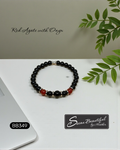Black Onyx and Red Agate beaded bracelet with Stainless Steel accents on a white surface with green leaves.