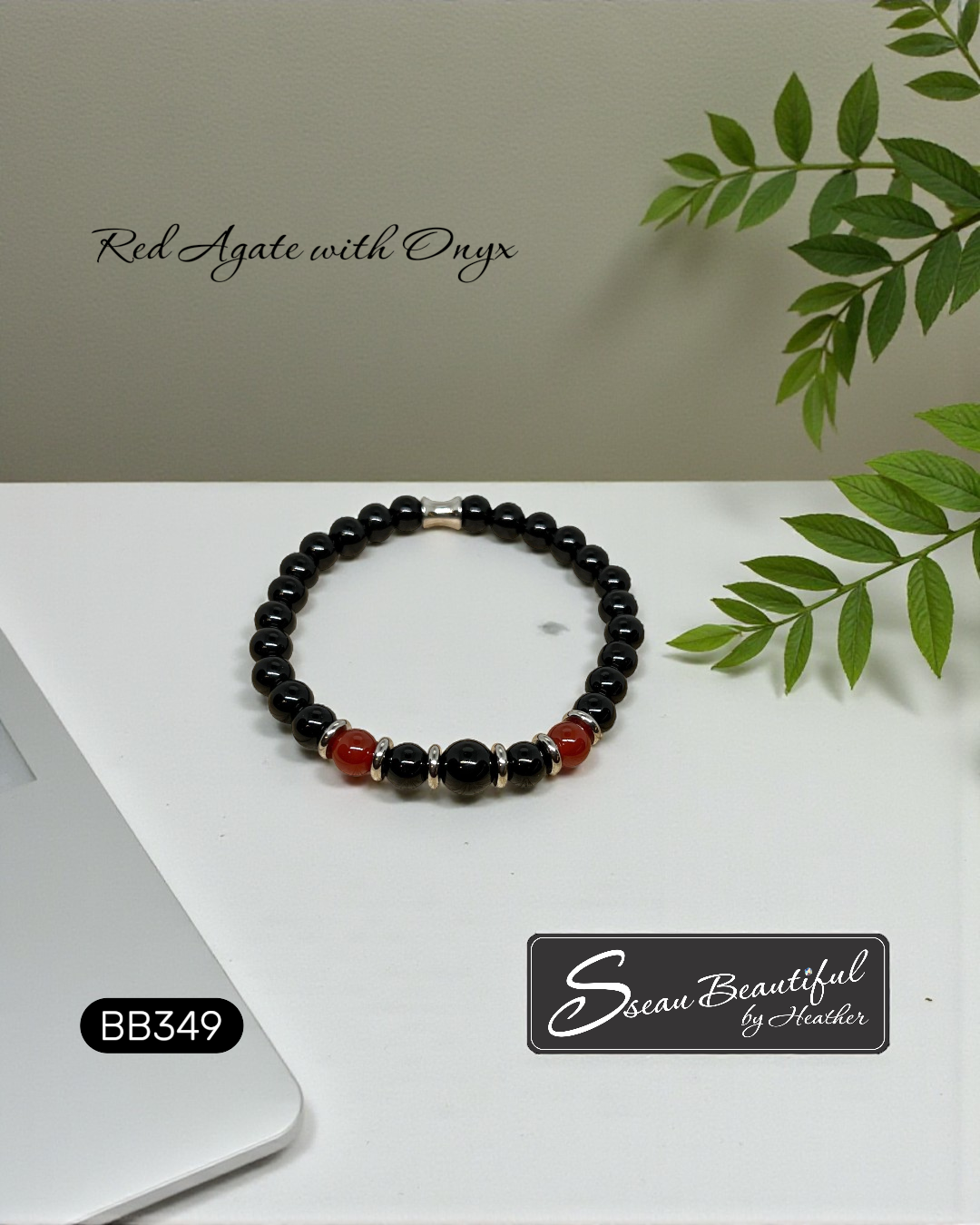 Black Onyx and Red Agate beaded bracelet with Stainless Steel accents on a white surface with green leaves.