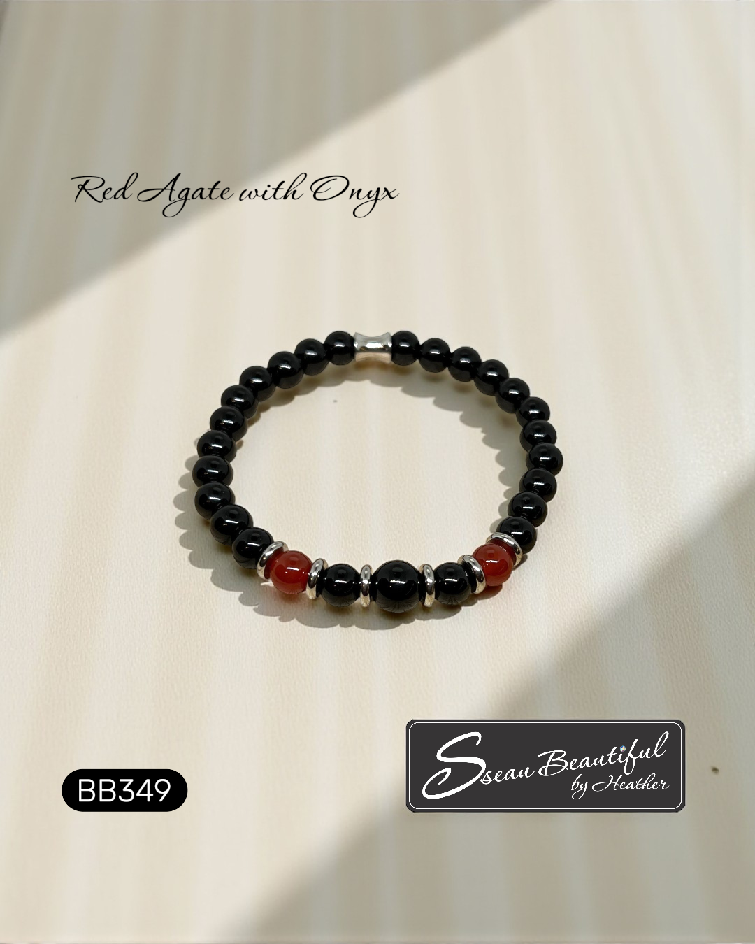 Black beaded bracelet with red agate and onyx on a beige background, featuring 'Sseau Beautiful by Heather' branding.