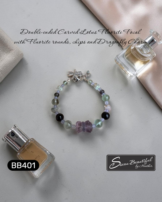 Photo of an adjustable bracelet strung with Fluorite round and chip beads featuring a double-ended carved Lotus Fluorite focal with a lobster clasp, extender, and a dragonfly charm, on a surface with nail polish and perfume; with descriptive text, "Sseau Beautiful"  logo and model number