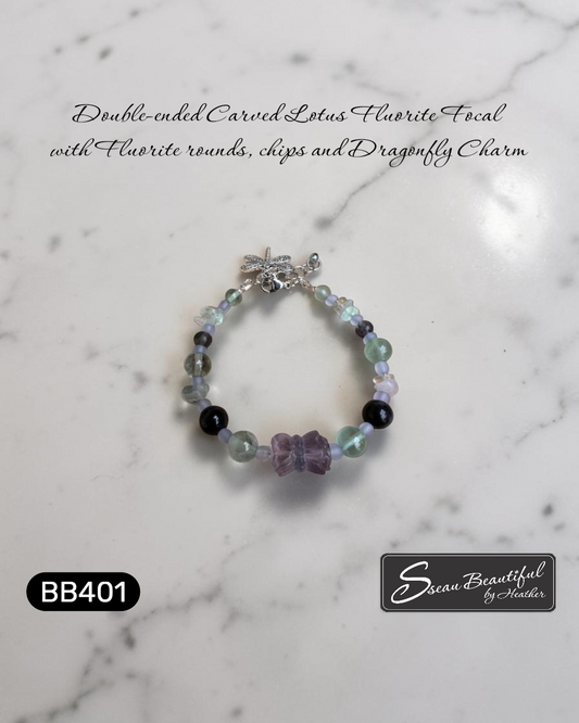 Photo of an adjustable bracelet strung with Fluorite round and chip beads featuring a double-ended carved Lotus Fluorite focal with a lobster clasp, extender, and a dragonfly charm, on a textured surface with descriptive text, "Sseau Beautiful" logo and model number