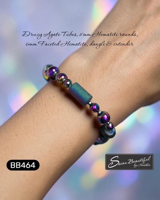 Bracelet with iridescent beads on a wrist against a blurred background, featuring branding text.