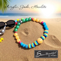 Colorful beaded necklace on sand with sunglasses and palm leaves, 'Sseau Beautiful' brand visible