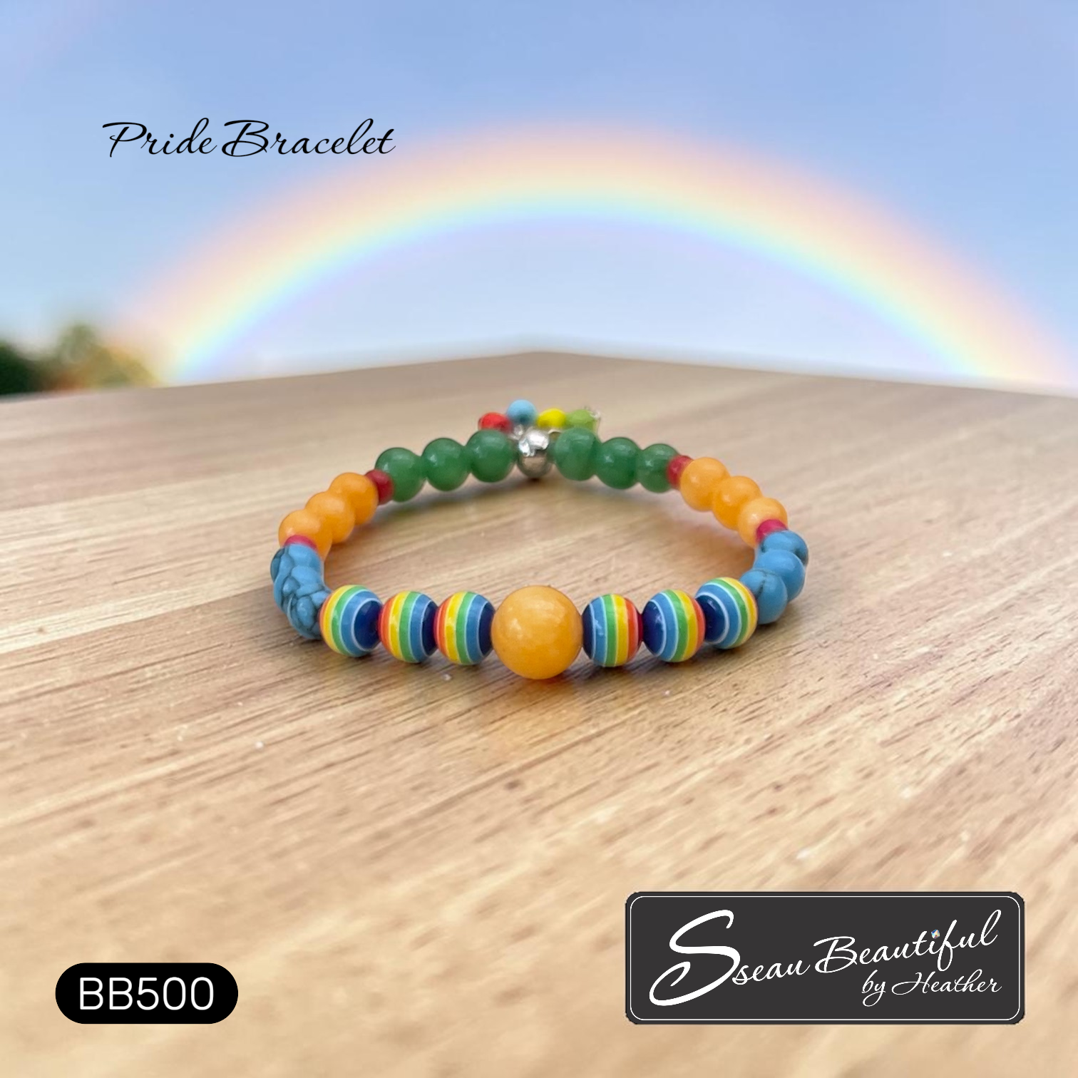 Colorful beaded bracelet on a wooden surface with a rainbow in the background, featuring the brand 'Sseau Beautiful by Heather'.