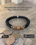 Black beaded bracelet with silver accents on a wood surface, featuring text about materials and brand.