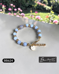 Adjustable bracelet with blue beads and gold accents on a white surface with blurred floral background