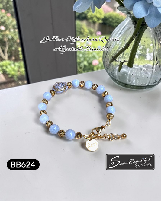 Bracelet with blue beads and gold accents on a white surface, featuring 'Sseau Beautiful by Heather' branding, next to a vase with blue flowers