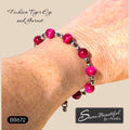 A close-up of a person's wrist wearing a beaded bracelet with bright fuchsia tiger eye and garnet beads separated by small silver stainless steel spacer beads. Text overlays read 'Fuchsia Tiger Eye and Garnet' and 'Sseau Beautiful by Heather', with a style code 'BB672'.
