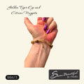 A hand with purple nail polish showing the clasp area of an adjustable bracelet shown against a cream background with text reading 'Golden Tiger Eye and Citrine Nuggets' and a brand label 'Sseau Beautiful by Heather'.