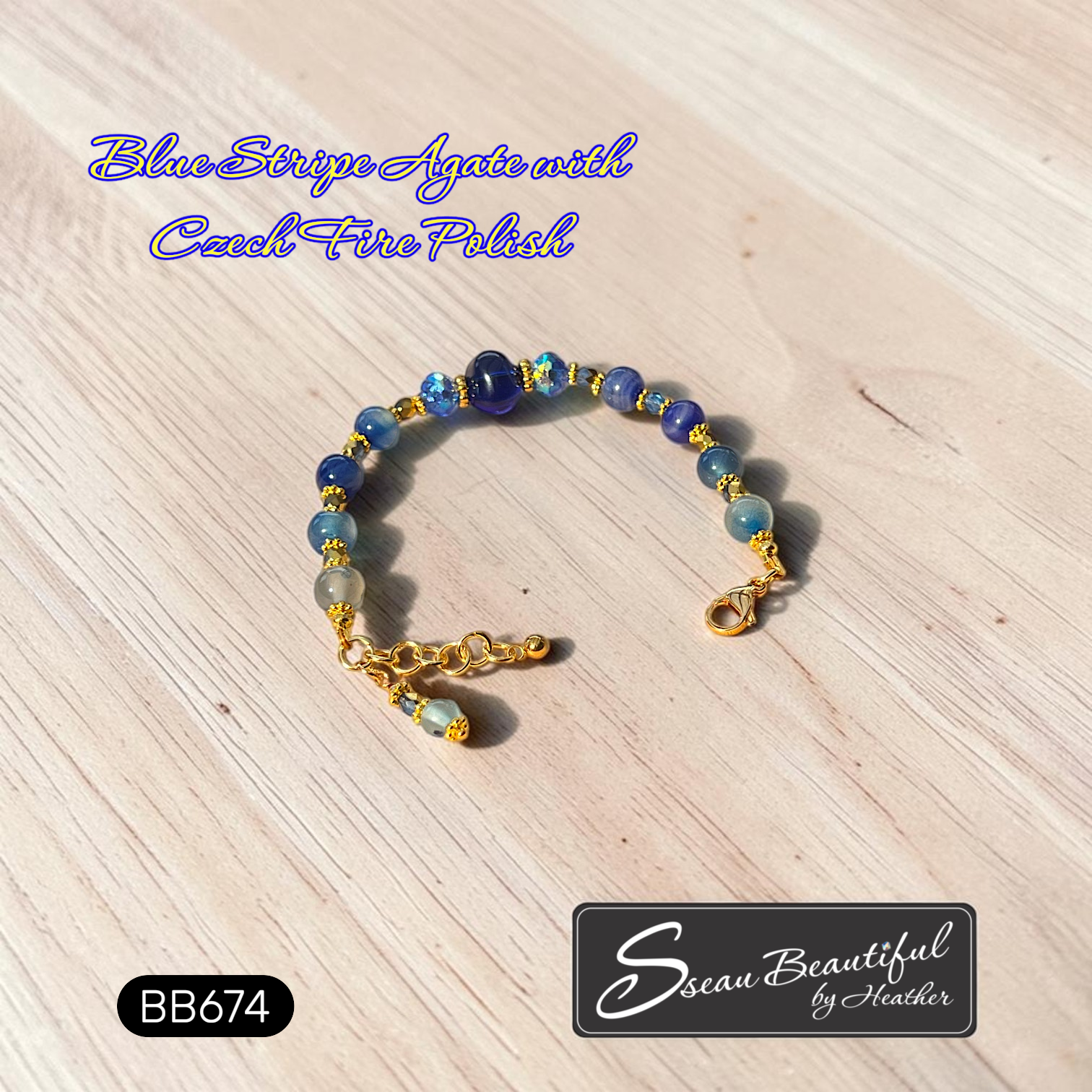 A beaded bracelet made of blue and light blue agate beads with gold spacer beads and a gold-tone Stainless Steel clasp, displayed on a light wood surface. Text overlays read 'Blue Stripe Agate with Czech Fire Polish' and 'BB674', with a logo for 'Sseau Beautiful by Heather' at the bottom right