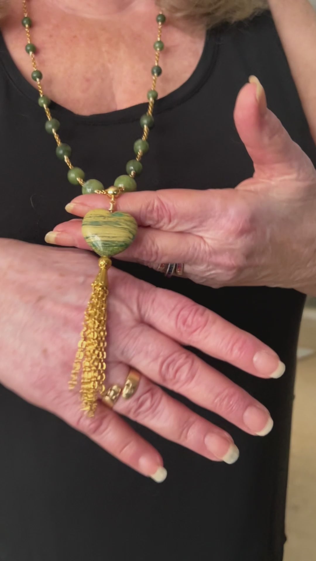 woman demonstrating swish-movement of the chain tassel on a green beaded necklace
