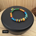 A colorful Pride Month stretch bracelet from Sseau Beautiful by Heather, featuring a yellow jade focal bead, rainbow acrylic beads, and gemstone accents, displayed on a rotating stand.