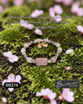 Sseau Beautiful! stretch bracelet with rose quartz, strawberry quartz focal, Czech crystals, and butterfly charm on mossy ground with pink blossoms.